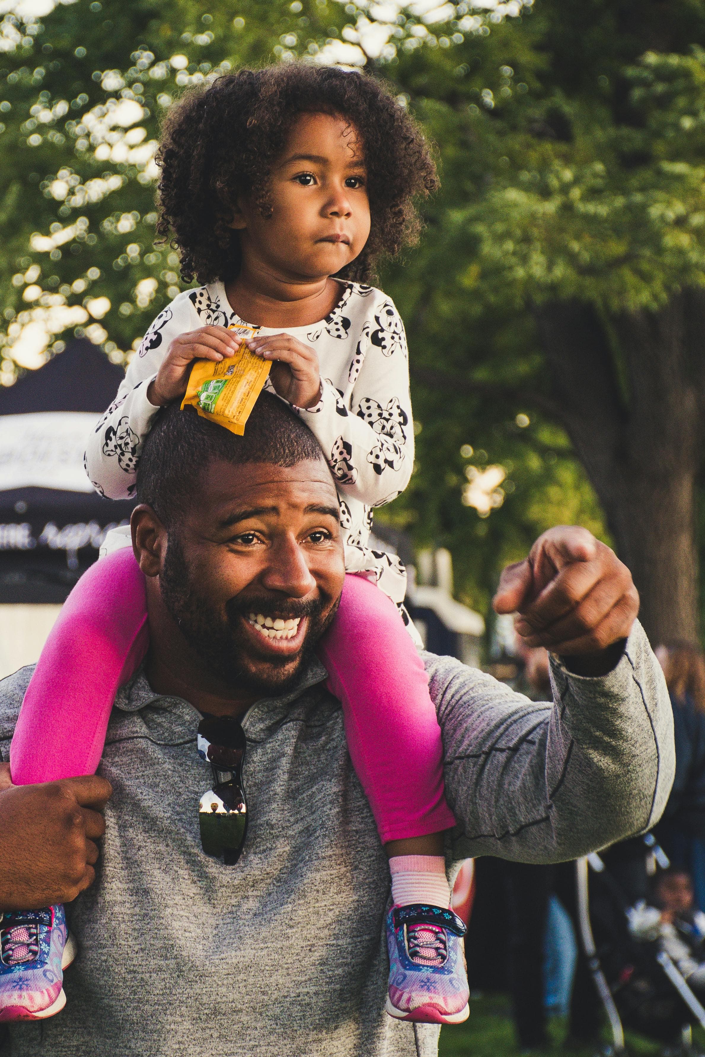 Free A joyful African American father with curly-haired daughter on shoulders, outdoors. Stock Photo