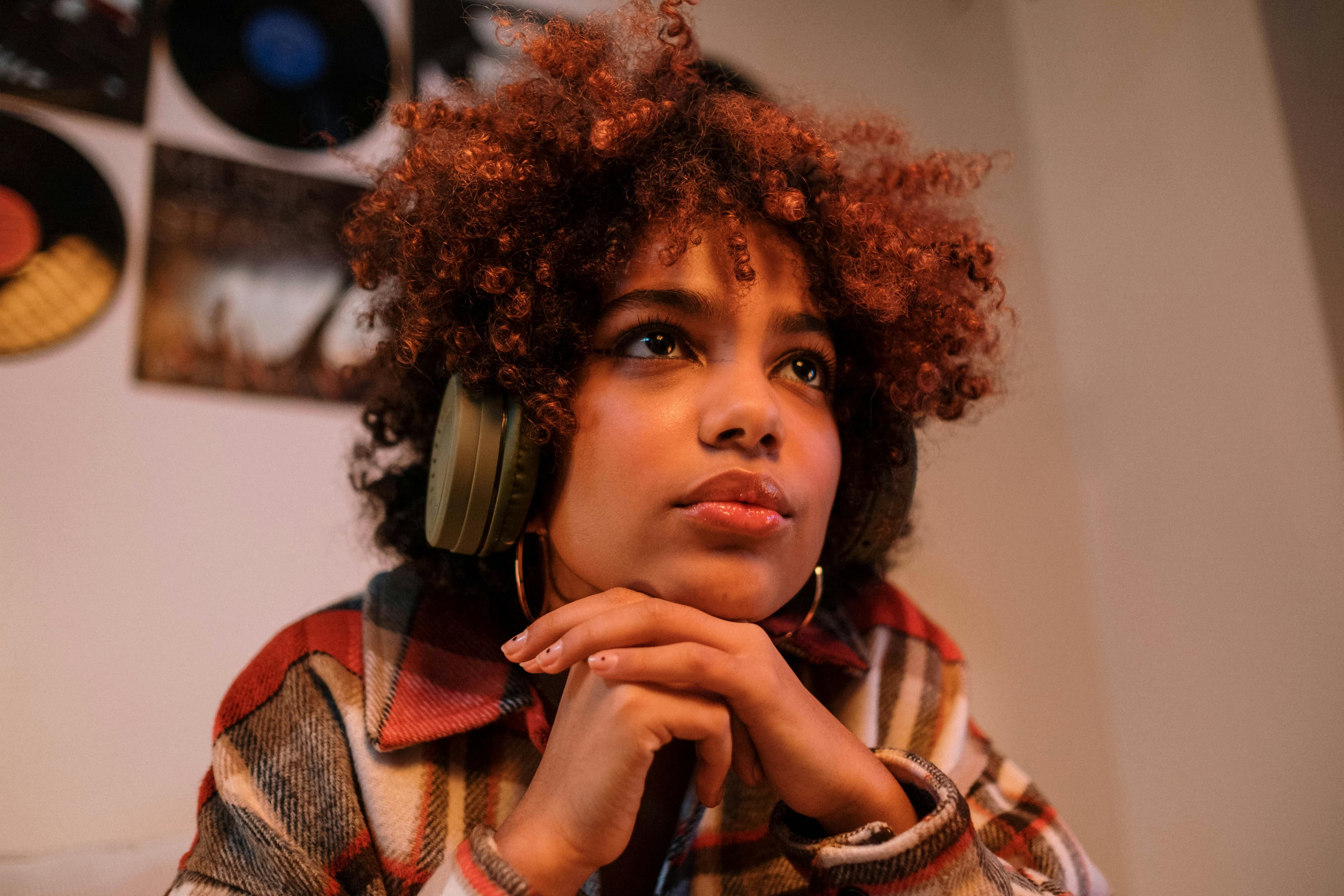 Free Thoughtful young woman with curly hair wearing headphones indoors, reflecting on music. Stock Photo