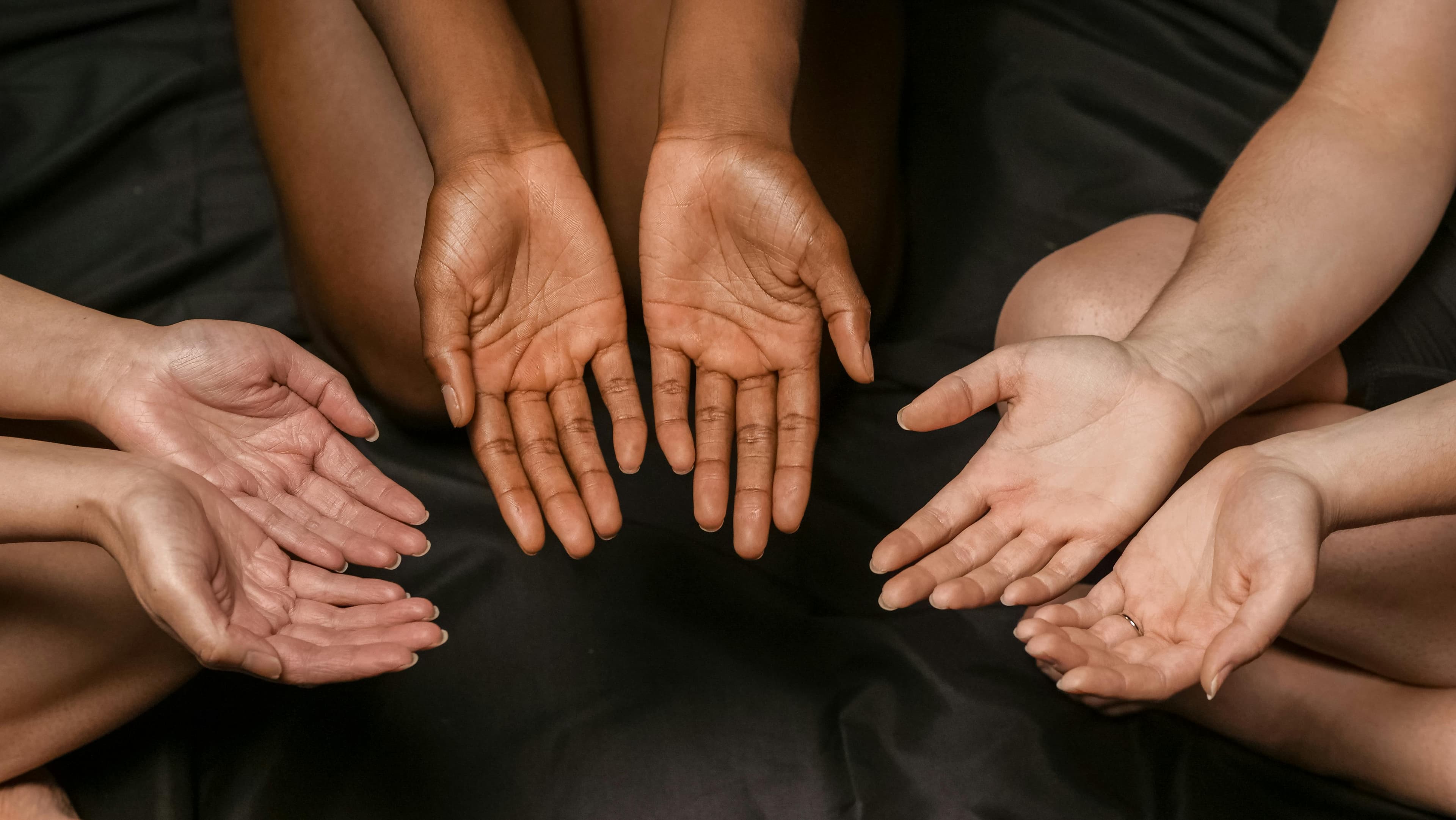 Free A close-up of diverse hands in a circular formation on a dark surface. Stock Photo